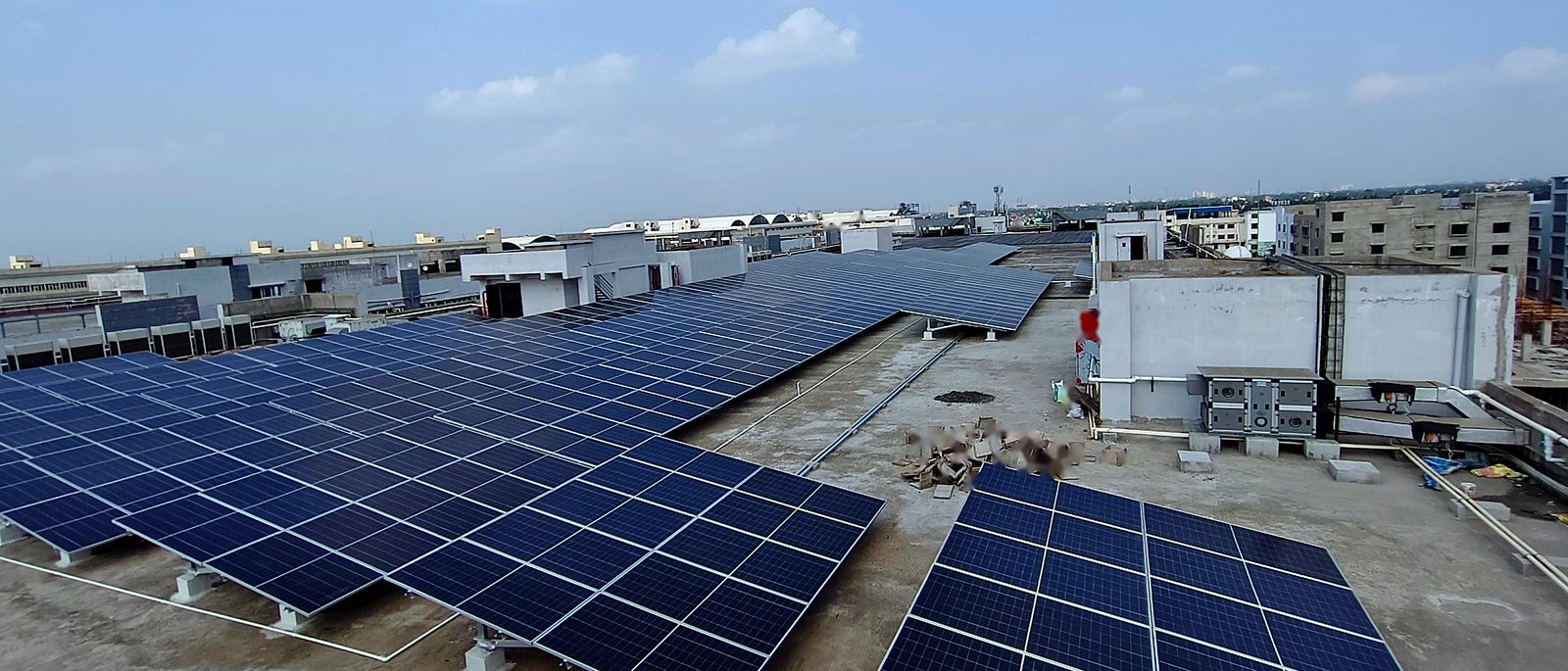 Commercial rooftop solar arrays installed across an industrial building, city skyline behind